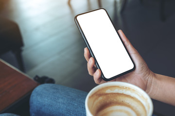 Mockup image of a hand holding black mobile phone with blank screen while drinking coffee in cafe