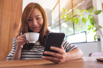 Closeup image of a woman holding , using and looking at smart phone while drinking coffee