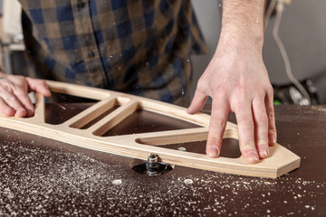 A young man carpenter builder equals a wooden bar with a milling machine in the workshop, in the background wooden boards