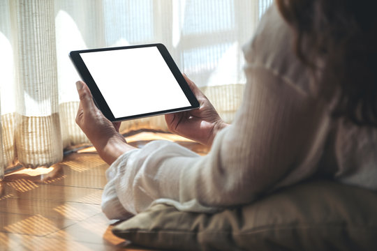 Mockup image of a woman holding black tablet pc with blank white desktop screen horizontally while laying down on the floor with feeling relaxed