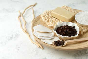 Set for anti-cellulite massage procedures. Coffee scrub, coffee grains, sea salt, soap, sponge on wooden plate and gray background, wellness homemade organic concept