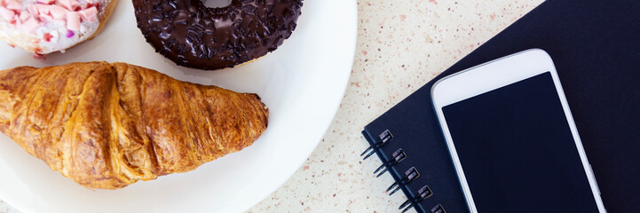work table with twirl and donut on white plate smartphone and blue notebook panorama