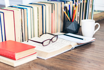 Stack of books education background, pencils, open book, glasses, and cup of tea with lemon.
