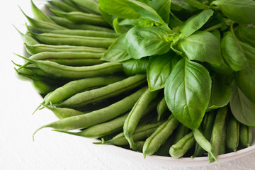 Thin French Green Beans (or Haricots Verts) with Basil Leaves on a Plate in White Background