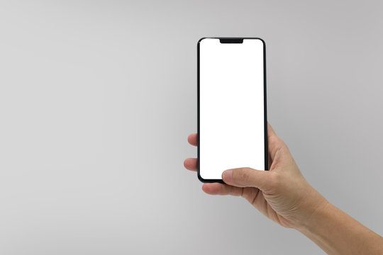 Hand holding black mobile phone with blank screen isolated on gray