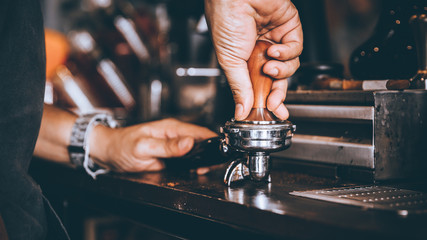 Professional Barista pressing tamping freshly ground coffee beans in a portafilter in coffee shop...