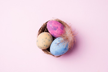 Colorful easter egg in the nest on pink background with copy space. Easter background. Minimalism