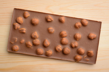 Bar of milk chocolate with nuts on light wooden background. Top view.