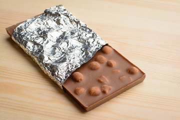 Bar of tasty chocolate with nuts covered with foil  lays on wooden table