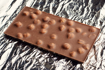 Bar of tasty milk chocolate with nuts lays on foil
