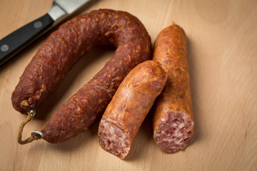 Luftgetrockneter Mettwurst Ring und frische Bierbeißer, zwei Salami Sorten aus Schweinefleisch mit Messer auf Holz Brett 