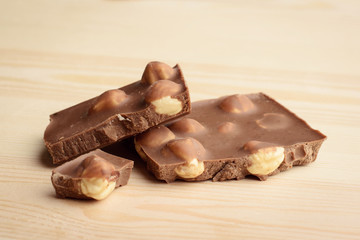Pieces of chocolate bar with a lot of hazelnuts on wooden background