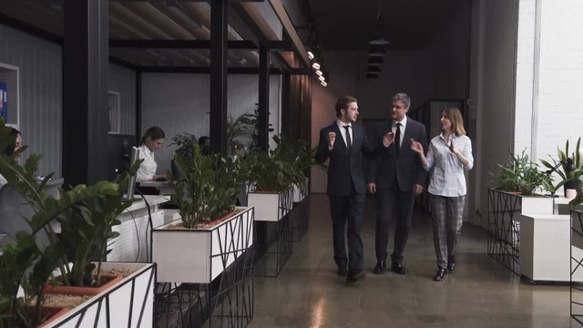  Mid-Aged Investor businessman walking with two corporate workers including businesswoman in the the office Interior. Discussing project or a contract. Giving promises and sharing expectations.