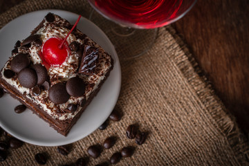 Black Forest Cake topping cherry putting on the white plate on the sack and wood background there are coffee bean and glass placed around.