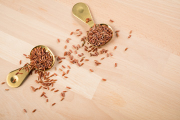 Rotschaliger roher roter Reis aus Piemont Italien und roter Jasmin Reis aus Kambodscha Asien in Metall Löffel auf Holz Hintergrund