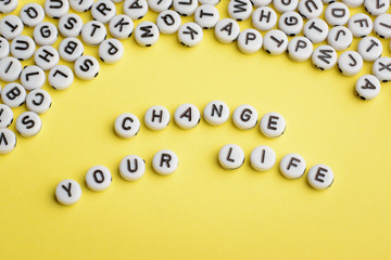 The expression CHANGE YOUR LIFE made of white plastic blocks on yellow background with many letters on the top