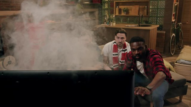 Close up slow motion view on four frustrated males sitting in front of broken smoky tv, the afro-american guy tries to repair it. Trouble, problem. Technology concept, home party, need a master