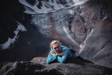 Woman traveler sitting on a rock high in the mountains on a glacier background. Tourism concept