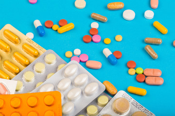 Different colorful pills and plastic packs - blisters stacked on blue abackground