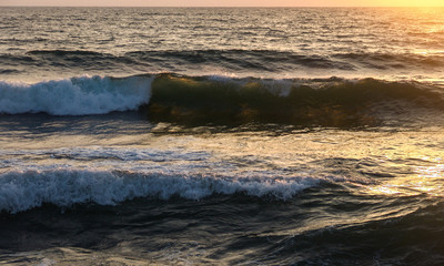Wave crashing in the sea, at sunset with water drops splashing and flying in the air and warm orange color from the sun