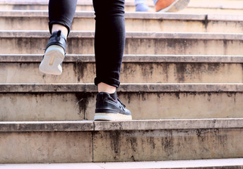 Fototapeta na wymiar Two legs of a person in sneakers climbing the stairs. A cropped shot, fragment, close-up, plenty of space for the text on the right. The concept of a healthy lifestyle.