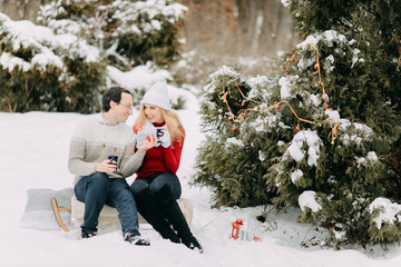 Happy couple in winter drinking tea and sitting on a sled