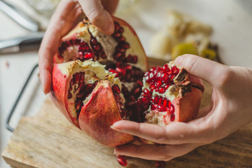 Young hands of a girl open a fresh juicy pomegranate - a healthy diet