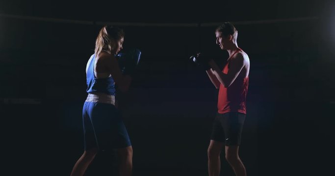 Beautiful brunette boxer working out blows to the paws with a trainer in a dark room