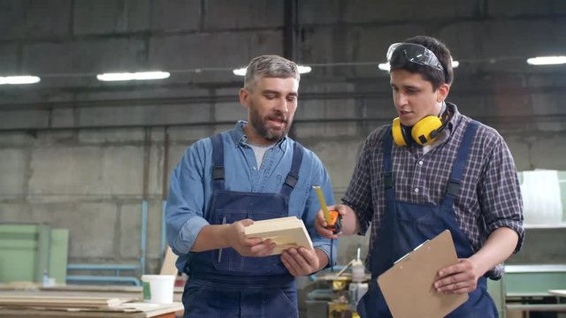 Following shot of two Caucasian joiners walking alone workshop and discussing wooden detail