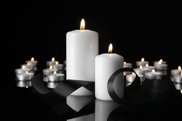 Burning candles and mourning ribbon on black background
