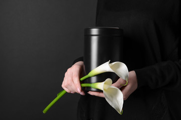 Woman with mortuary urn and flowers on dark background, closeup