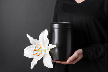 Woman with mortuary urn and lily flower on dark background, closeup