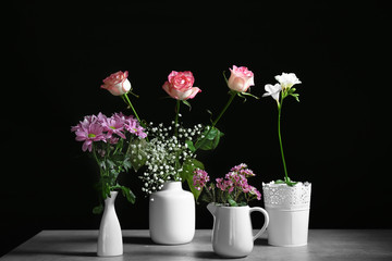 Vases with beautiful flowers on table against dark background