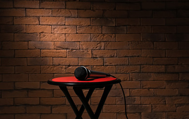 Modern microphone on stool against brick background