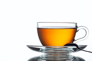 A cup of black tea and a spoon on a white table with reflection