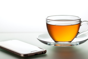 A cup of black tea and a spoon on a white table with reflection