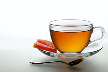 A cup of black tea and a spoon on a white table with reflection