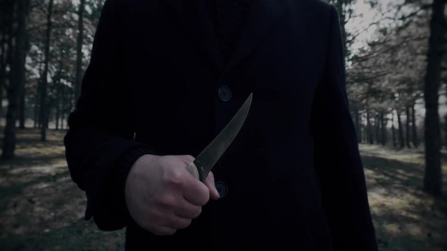 Dangerous killer with knife pursues victim and looking for her in woods in close up