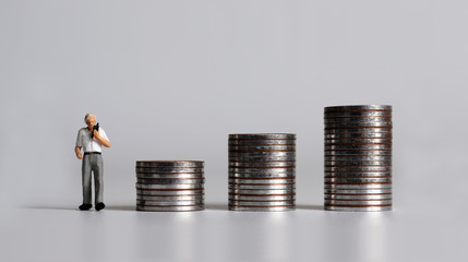 A miniature man with three piles of coins and a cell phone.