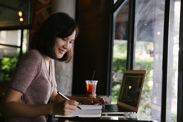 Young business woman in casual dress sitting at table in cafe and writing in notebook.