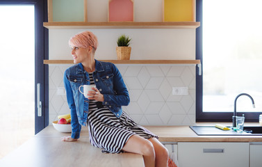 Fototapeta premium A young attractive woman sitting on a counter in a kitchen at home.