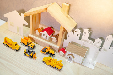 House models, paper crane and city background with miniature yellow trucks on wooden table. Architecture and construction industry for housing development business. Property or real estate concept