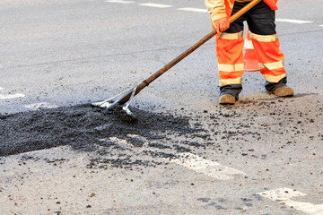 A road builder collects fresh asphalt on part of the road and levels it for repair in road...