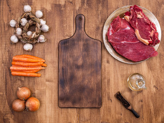 Top view of vintage cutting board next to two pieces of red meat on wooden table