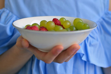 Hand holding bowl with grapes and raspberries