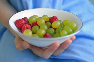 Hand holding bowl with grapes and raspberries