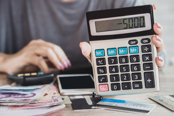 woman hand holding calculator with budget deficit for credit card debt payment with some banknotes...