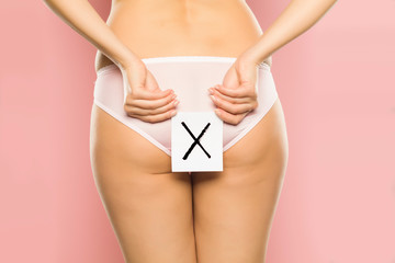 Woman holding paper with X sign in front of her buttocks