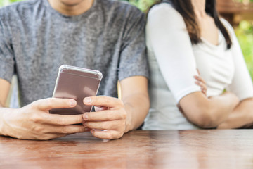 boyfriend using smartphone with upset girlfriend sitting beside ,social ignorance, and social addiction concept 