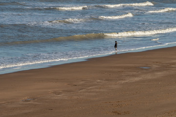 Lone boy standing on the beach with his feet in the sea